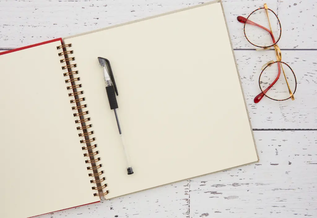 Un stylo, un carnet ouvert et des lunettes sur un bureau clair
